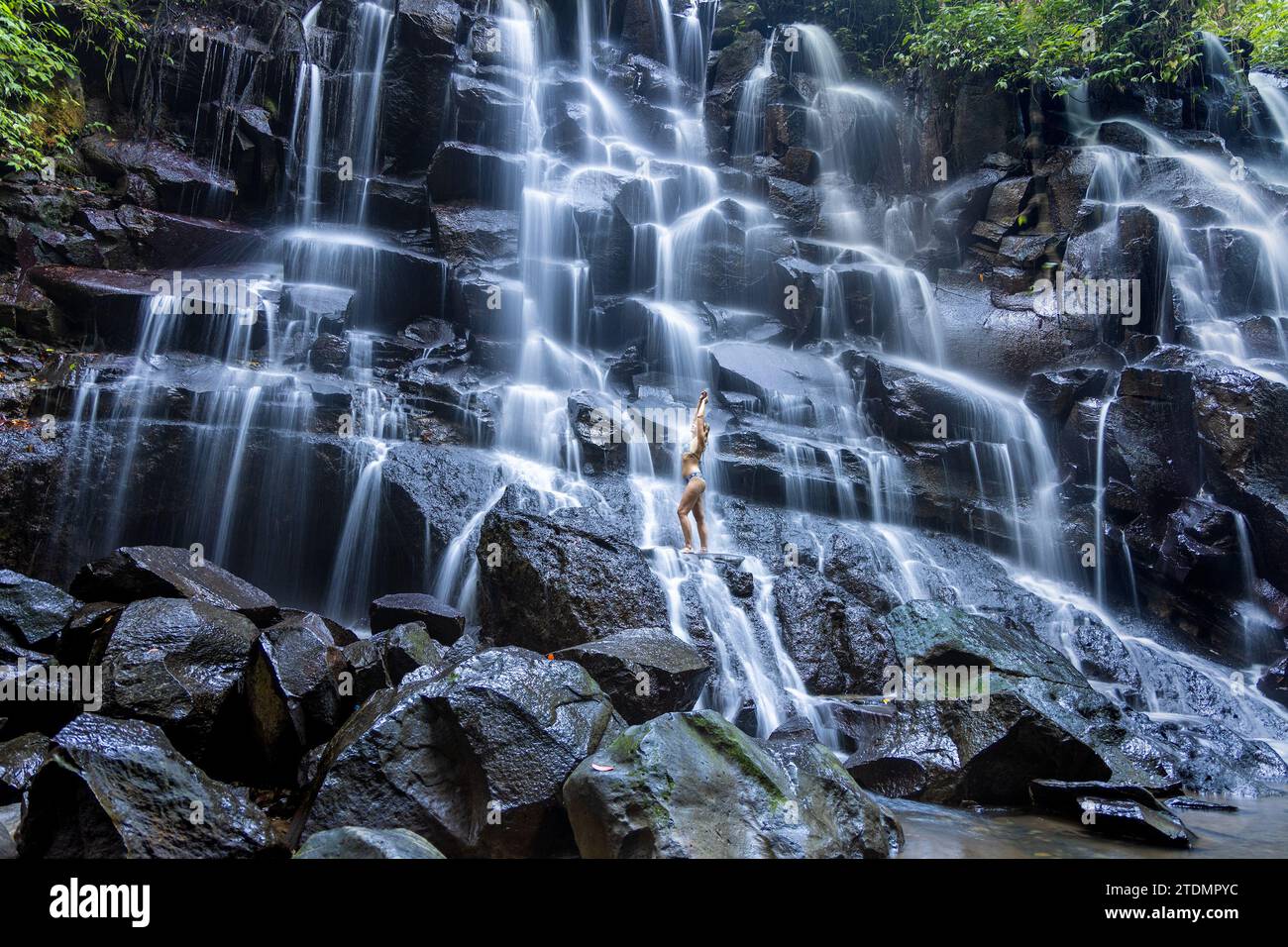 Eine junge Frau im Badeanzug am Kanto Lampo Wasserfall im üppigen tropischen Wald, Bali, Indonesien Stockfoto