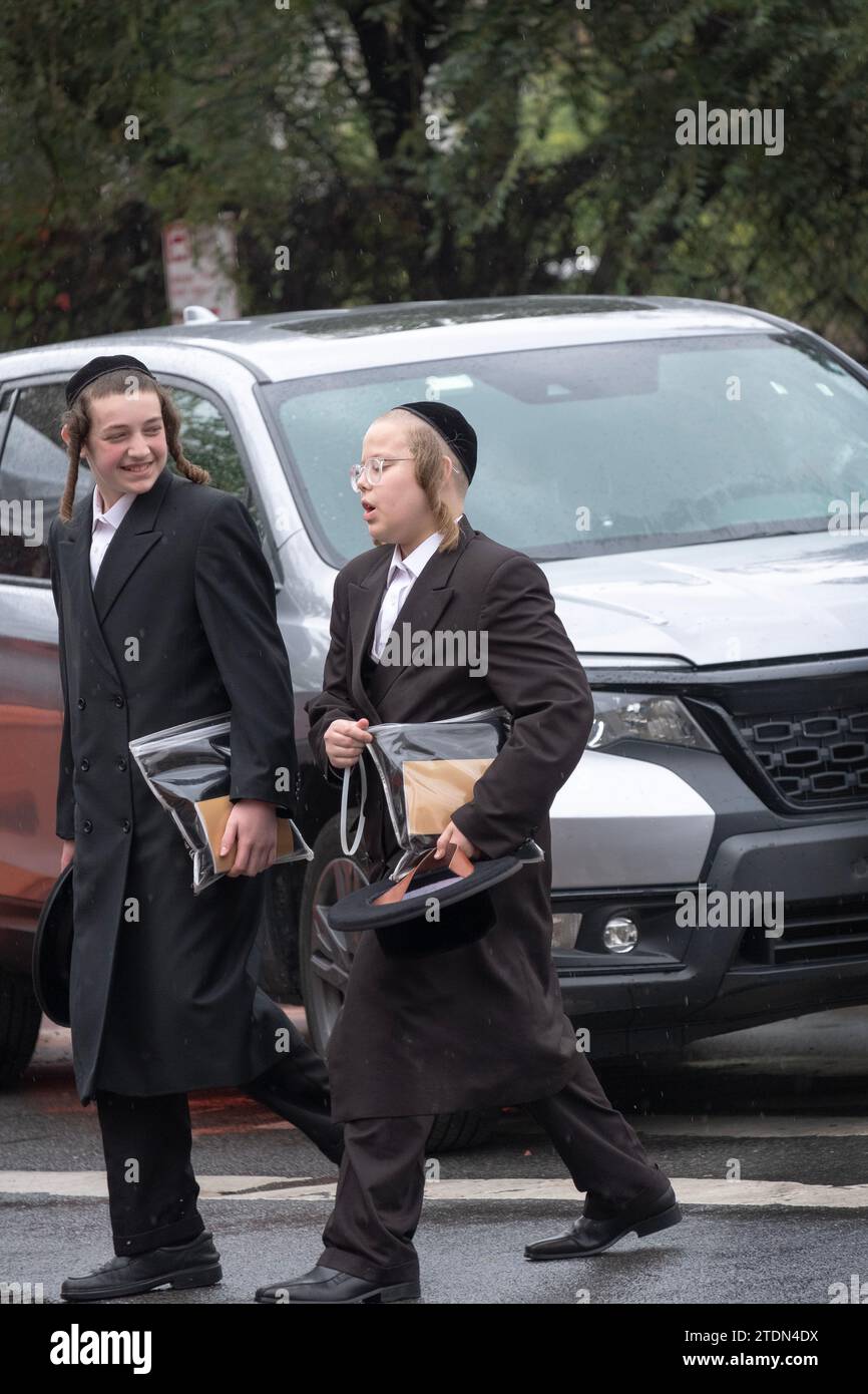 2 chassidische Teenager in schwarz gekleidet unterhalten und lachen nach den Morgengottesdiensten in Williamsburg, Brooklyn, New York. Stockfoto