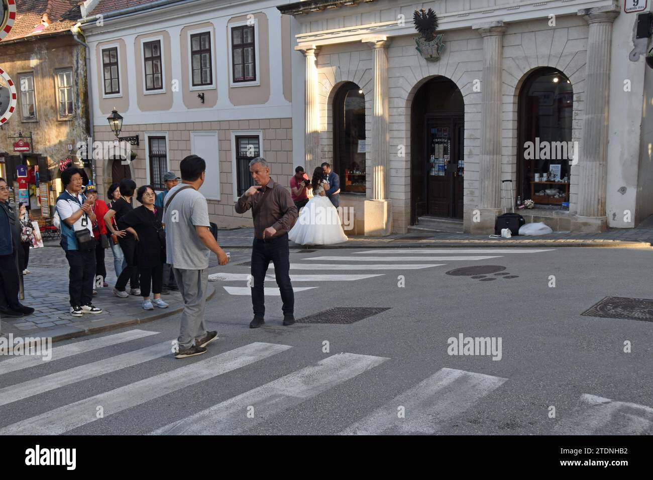 Touristen auf einer geführten Tour mit einem Paar, das im Hintergrund Hochzeitsfotos in der Altstadt von Zagreb, Kroatien, gemacht hat Stockfoto