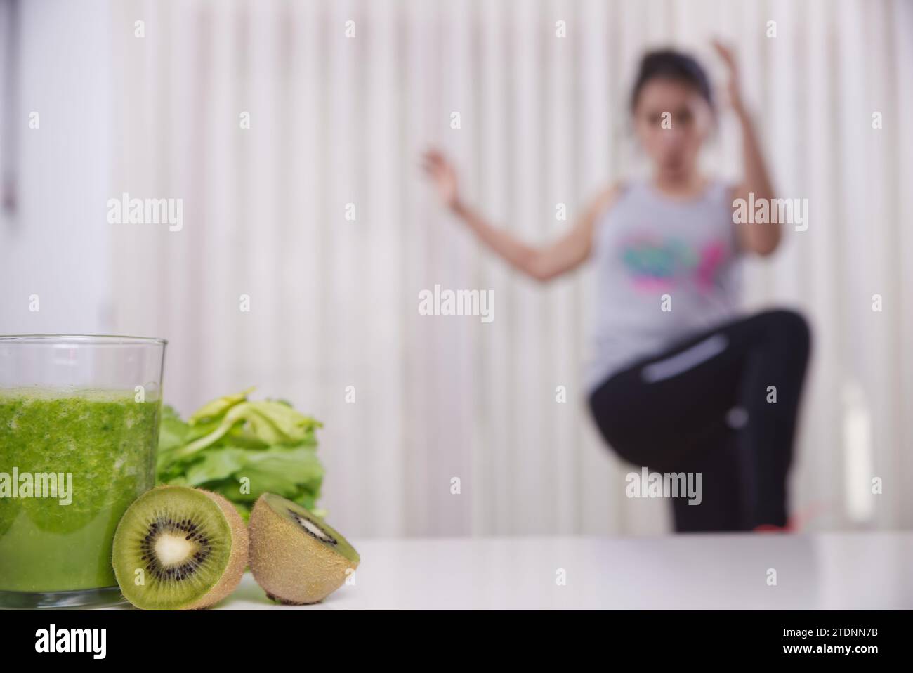 Grüner Smoothie mit fokussierten Kiwis und Frau, die unfokussiert trainiert Hintergrund Stockfoto