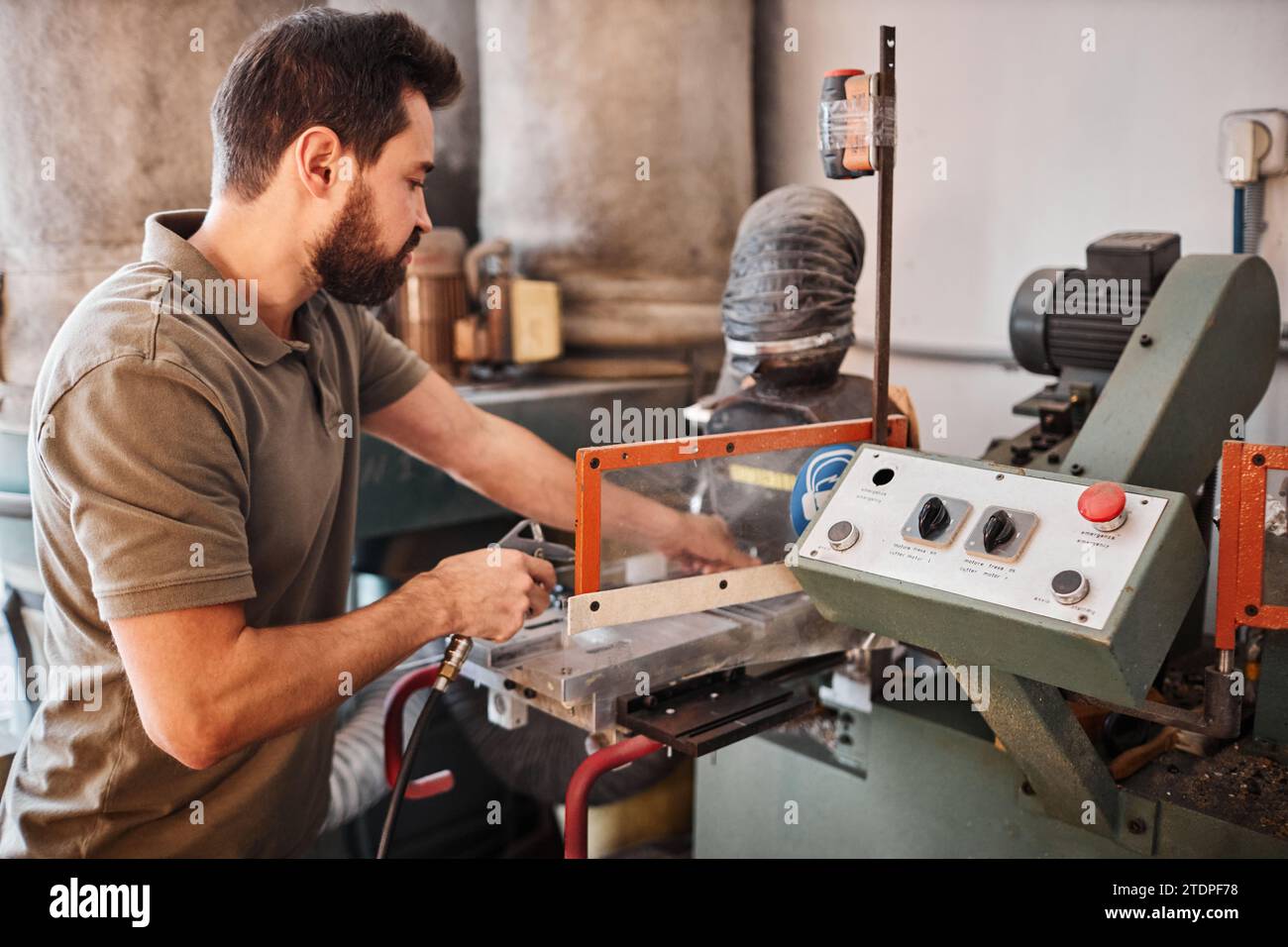 Junger männlicher Hersteller, der industrielle Maschinen für die Schuhherstellung verwendet, während er Leder oder unfertige Schuhe in der Werkstatt verarbeitet Stockfoto