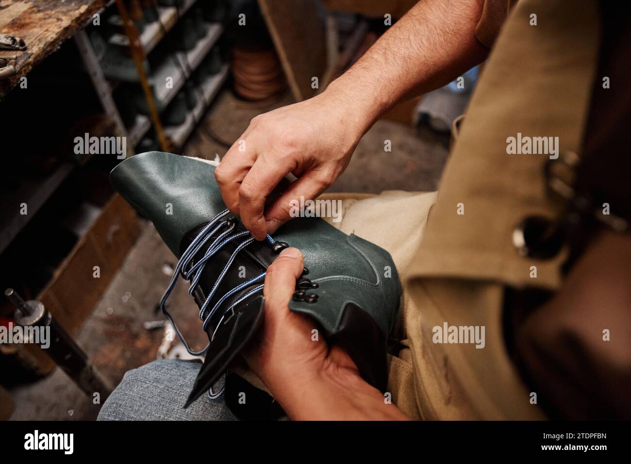 Hände eines professionellen männlichen Schuhmachers, der Schnürsenkel in den oberen Teil des unfertigen schwarzen Lederstiefels steckt, während er in der Werkstatt sitzt Stockfoto