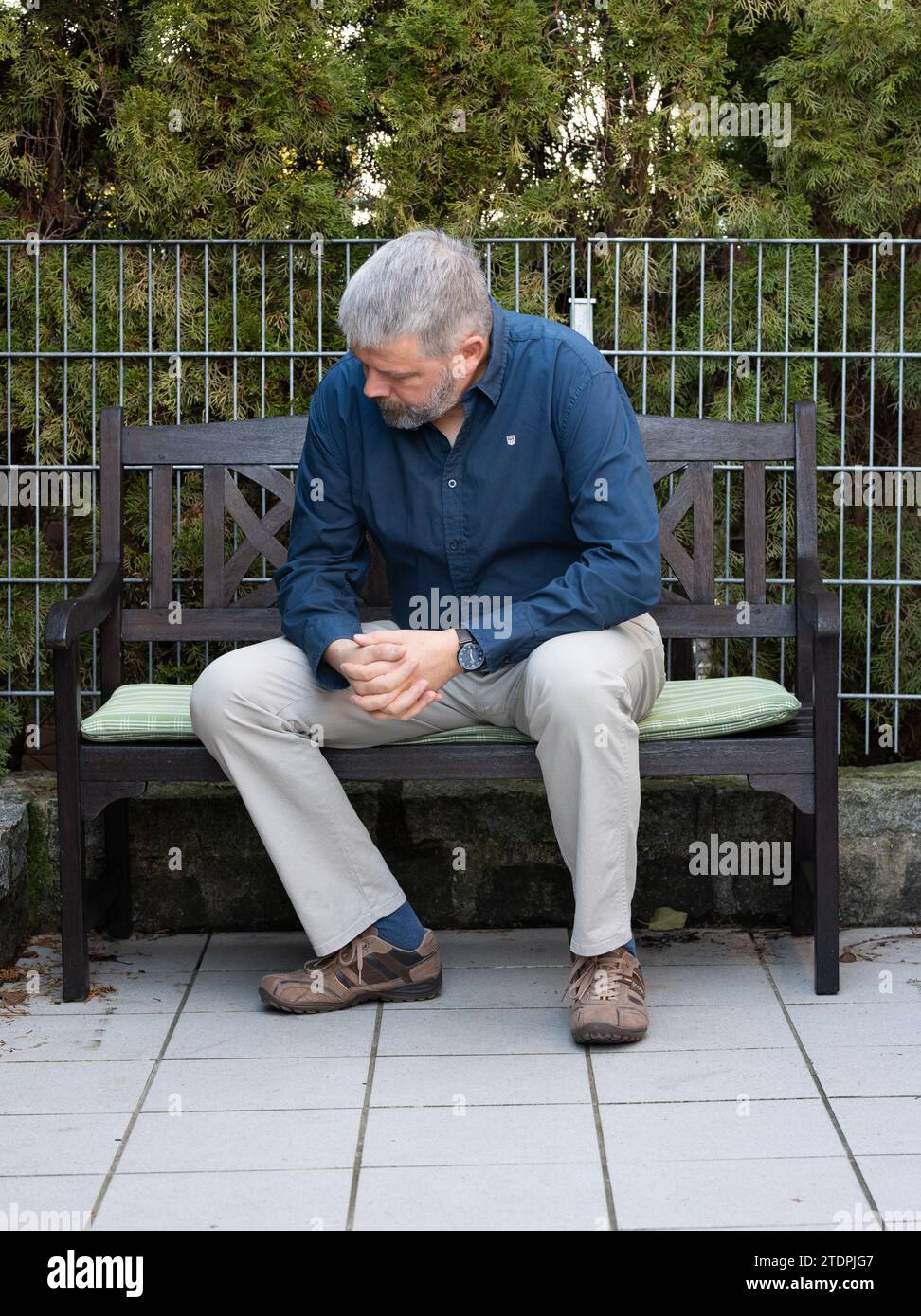 Mann mit grauen Haaren und Vollbart, 50-59 Jahre alt, sitzt auf einer Bank auf der Terrasse, hängt seinen Kopf, nachdenklich, traurig Stockfoto