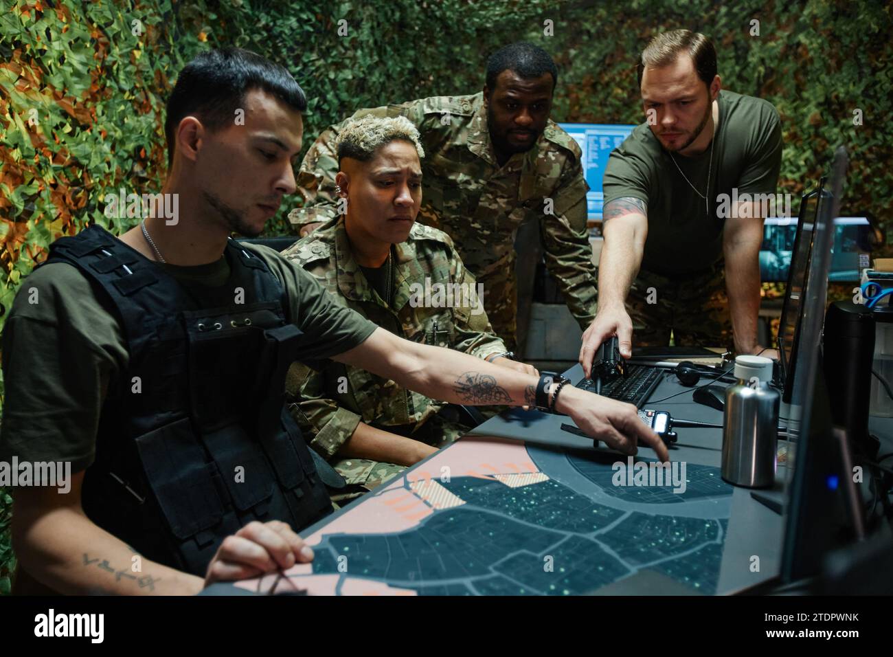 Gruppe junger interkultureller Offiziere in Uniform, die sich die Karte ansehen und darauf zeigen, während sie Taktiken und Strategien der Armee diskutieren Stockfoto