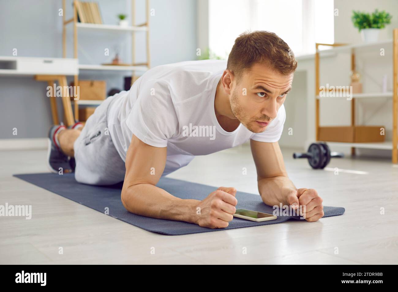 Junger attraktiver Mann, der Plank-Übungen macht, liegend auf Yogamatte auf dem Boden zu Hause. Stockfoto