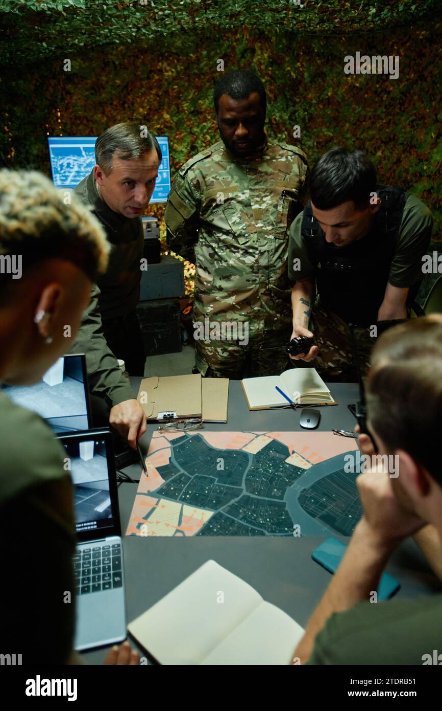 Gruppe junger interkultureller Soldaten, die sich die Karte ansehen, während sie am Arbeitsplatz stehen und militärische Strategien und Taktiken diskutieren Stockfoto