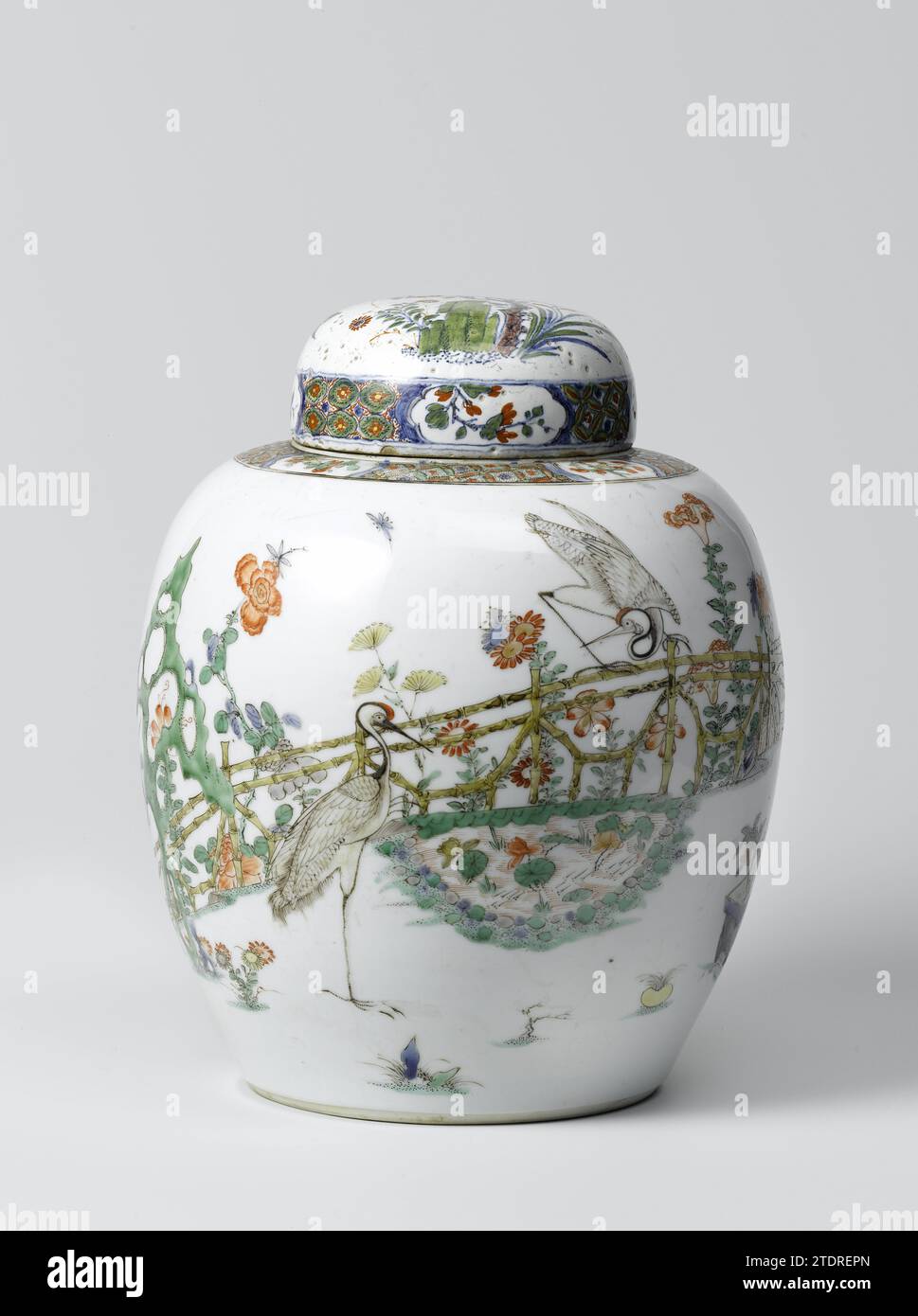 Deckelglas, anonym, ca. 1700 - ca. 1720 Ei-förmiger Deckeltopf aus Porzellan, bemalt auf der Glasur in Blau, Rot, Grün, Gelb, Aubergine und Schwarz. An der Mauer ein umzäunter Garten mit zwei Kranichen, einer stehend und einer auf dem Zaun, in der Nähe eines Teichs mit Lotuspflanzen, einem Felsen und einem blühenden Baum (Magnolie). Rund um den Teich blühende Pflanzen (Chrysantheme, Splendid, Pfingstrose, Aster, Lilie) und zwei Blumentöpfe mit Kiefer, Bambus und Orange. Im Magnolienbaum ein Papagei auf einem Gestell. Außerdem zwei fliegende Vögel. Auf der Schulter Servetarbeit durchsetzt mit Blumenzweigen in Kartuschen. Der Deckel wurde später in t hergestellt Stockfoto