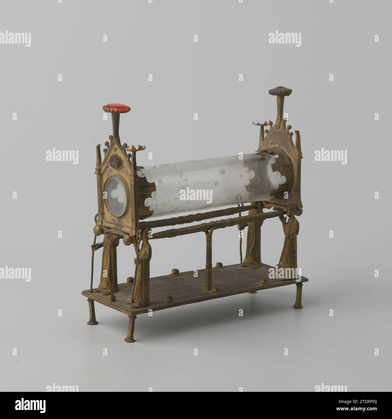 Reliek-Oostensorium, Anonym, um 1800 - um 1900 das Objekt aus vergoldetem Kupfer besteht aus einer Platte mit einer gravierten Christusfigur, die auf vier Beinen und mit zwei Gaffelstandards in der Mitte platziert ist, von denen einer fehlt. An den Ecken befinden sich vier Bischöfe mit den Köpfen in der gleichen Richtung und jeder mit einer Krähe in der Hand. Zusammen mit den Gaffel-Standards tragen sie ein zylindrisches Glas in einem vergoldeten Kupferrahmen, bestehend aus zwei erhöhten Platten und zwei horizontal platzierten Stiften, die das Zylinderglas tragen. Die Verkleidungen des Rahmens sind mit Stockfoto