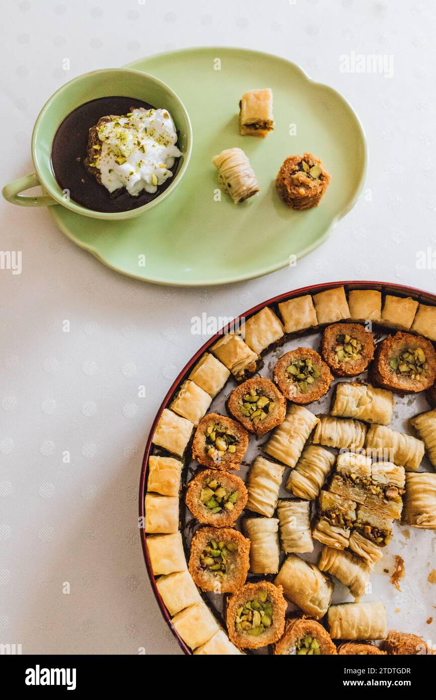 Heiße, trinkende Schokolade in passender grüner Tasse und Teller mit verschiedenen Baklava-Desserts auf weißem Polka Dot Tischtuch Stockfoto