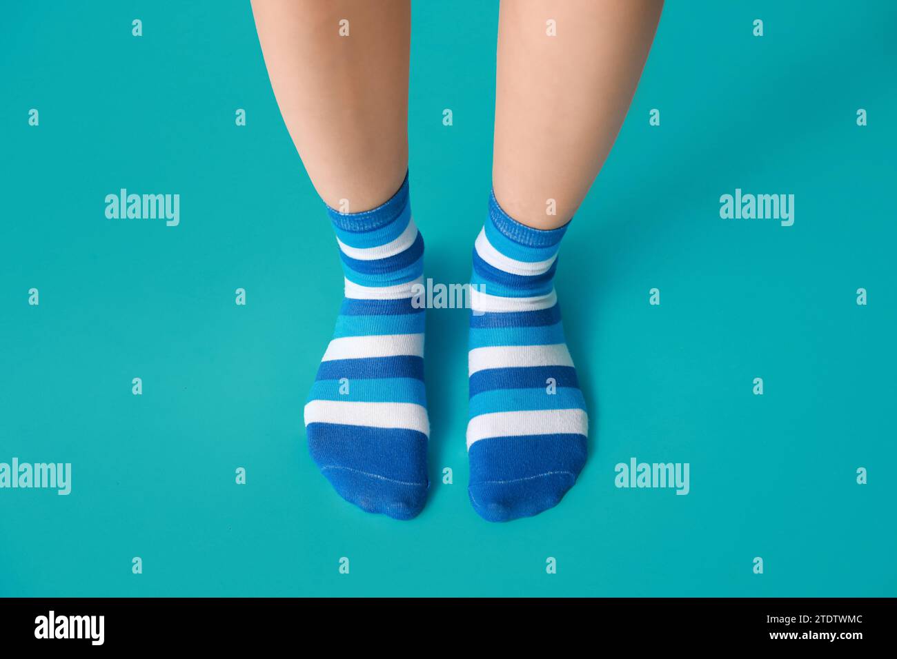 Beine einer jungen Frau in gestreiften Socken auf blauem Hintergrund Stockfoto