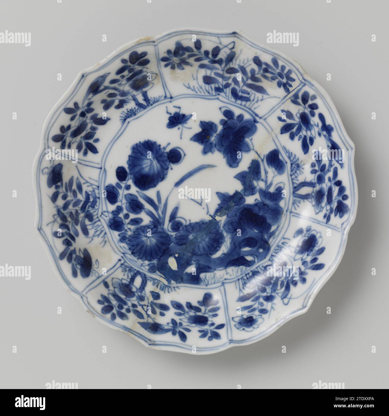 Untertasse mit Felsen, Blumensprays und Schmetterlingen, anonym, ca. 1700 - ca. 1724 Untertasse aus Porzellan mit geriffelter Wand und gewelltem Rand, in Unterlaze blau lackiert. Auf der Ebene ein Fels mit zwei Blütenzweigen (Chrysantheme, Pfingstrose) und einem Schmetterling; die Mauer unterteilt sich in sechs Abteilungen mit Blumensträngen und Vögeln; drei Blumenzweige auf der Rückseite. Auf der Unterseite mit einer Dichtungsmarke in einem Doppelkreis gekennzeichnet. Das Gericht ist kaputt. Blau Weiß. Porzellan. Glasur. Kobalt-(Mineral-)Malerei / Glasur Untertasse aus Porzellan mit geriffelter Wand und gewelltem Rand, in Unterlazeblaze blau lackiert. O Stockfoto