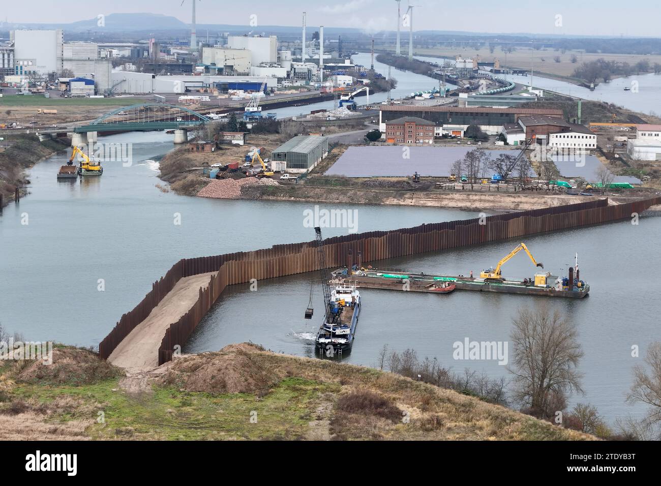 18. Dezember 2023, Sachsen-Anhalt, Magdeburg: Blick auf die Baustelle vom neuen Damm im Magdeburger Industriehafen (Luftaufnahme mit Drohne). Der Hafen Magdeburg will den Industriehafen bis 2024 erweitern und damit bessere Voraussetzungen schaffen, um das jährliche Umschlagsvolumen zu erhöhen. Bis zum Kanalhafen mit seinem Trenndamm kann der Hafen unabhängig vom Wasserstand der Elbe genutzt werden, da der Zugang vom Mittellandkanal möglich ist. Die Wassermangelsicherung und die Wassermangelsicherung regulieren den Wasserstand. Der Industriehafen hatte jedoch noch direkten Zugang zur Elbe und ist somit dep Stockfoto