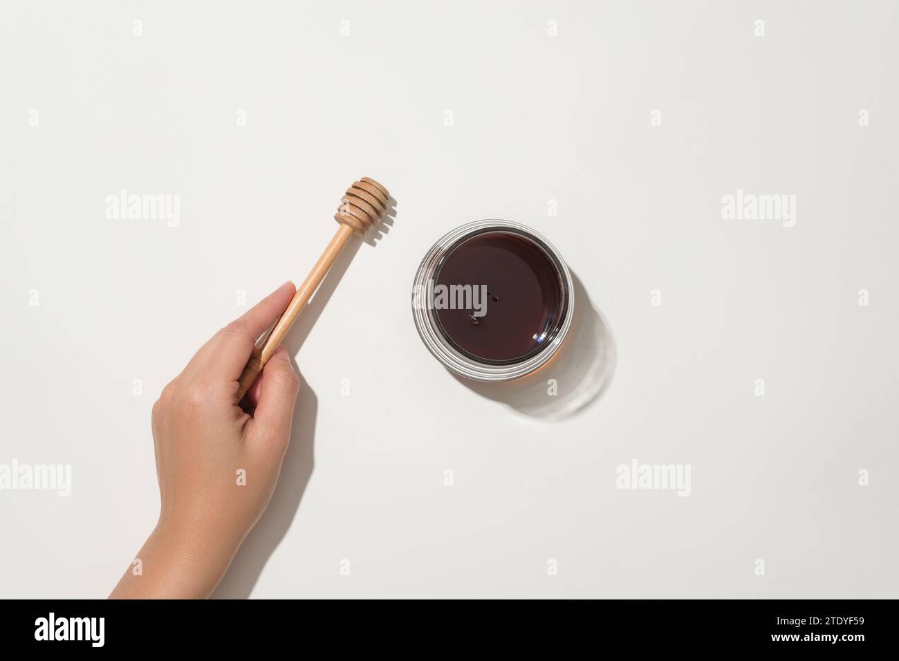 Hand hält einen Honig-Niesel, neben einem Glas Honig auf weißem Hintergrund. Honig hilft effektiv, die Poren zu straffen. Der Nutzen des Honigs. Stockfoto