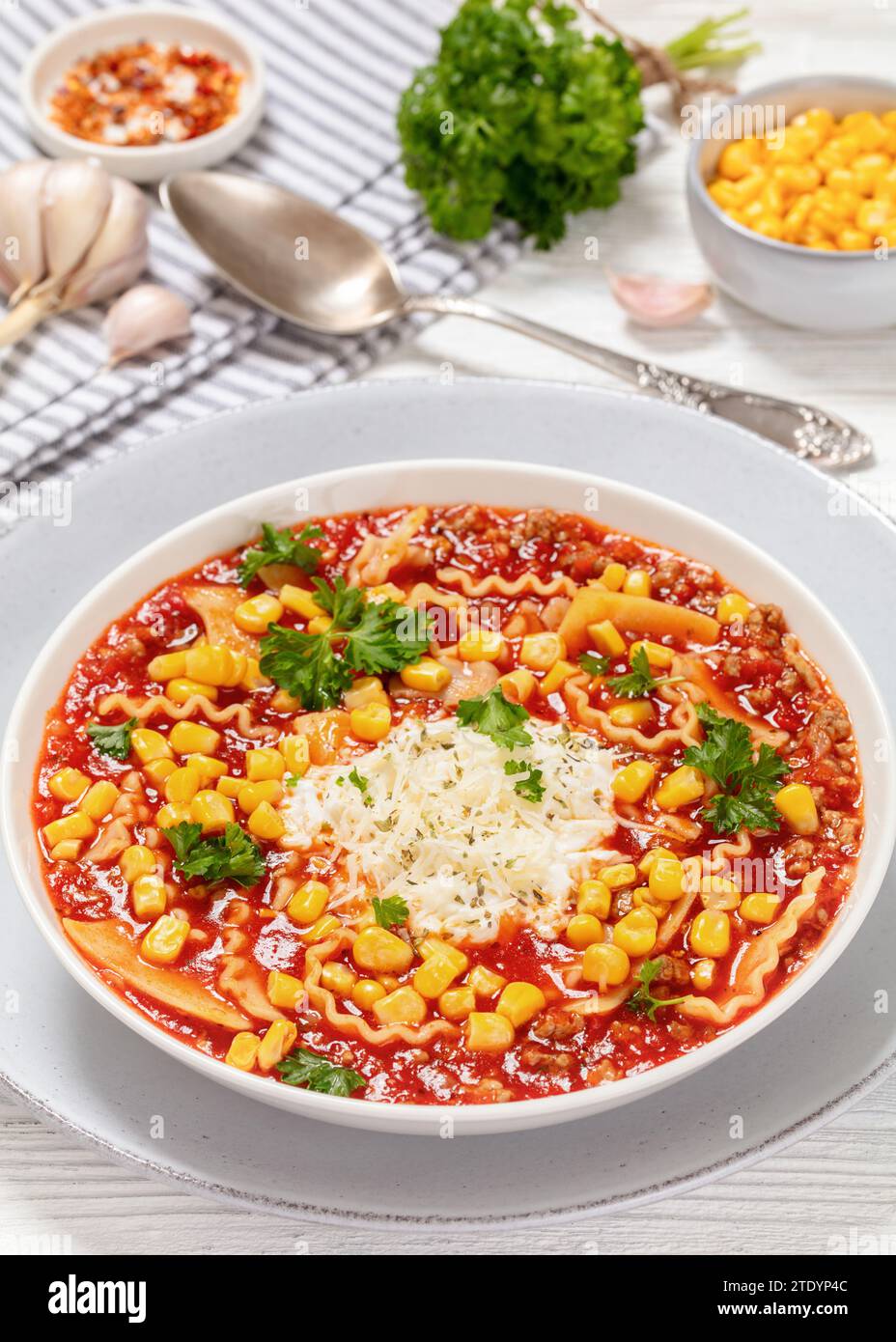 Lasagne-Suppe vom Hackfleisch, Lasagnudeln, Tomaten, Mais, Gewürze, Ricotta- und Parmesankäse in weißer Schüssel auf weißem Holztisch, vertikale Ansicht, Stockfoto