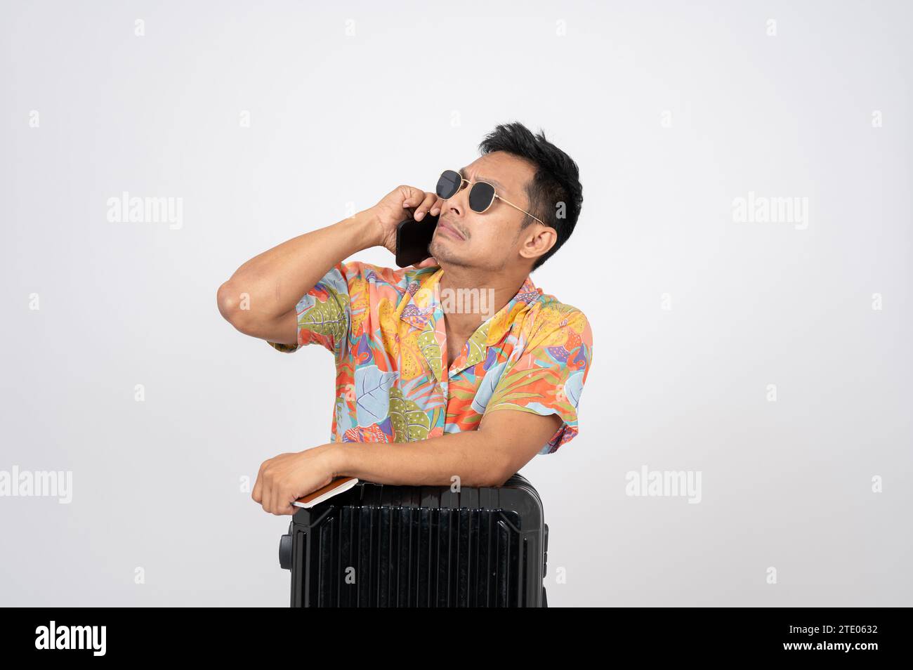 Ein trauriger asiatischer Tourist in Sommerkleidung spricht am Telefon mit jemandem auf einem isolierten weißen Hintergrund. Ich habe den Flug verpasst, da ich Probleme hatte Stockfoto