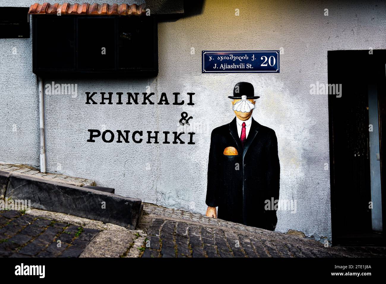 Straßengemälde mit einem Mann in Hut und Anzug mit Khinkali für ein Gesicht vor dem Khinkali & Ponchiki Restaurant in der Nähe der Zitadelle von Narikala in Tiflis, Georgia Stockfoto