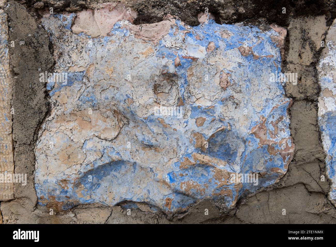 Abstraktes Detail der äußeren Steinmauer eines Gebäudes, das alte Schichten von gerissener und abblätternder Farbe freilegt. Stockfoto