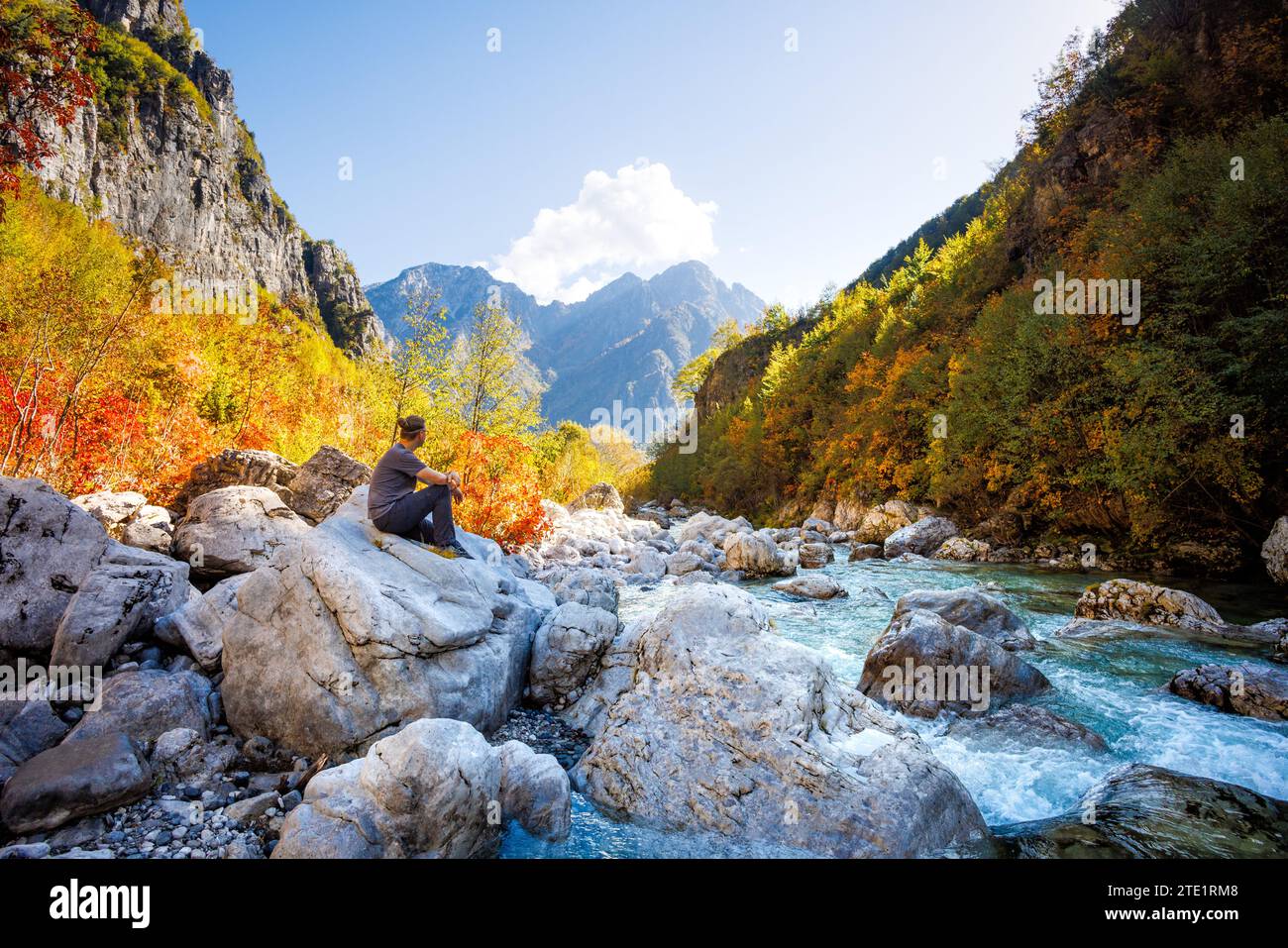 Mann, der auf einem Felsen in der Nähe eines Flusses in den bunten albanischen Alpen sitzt Stockfoto