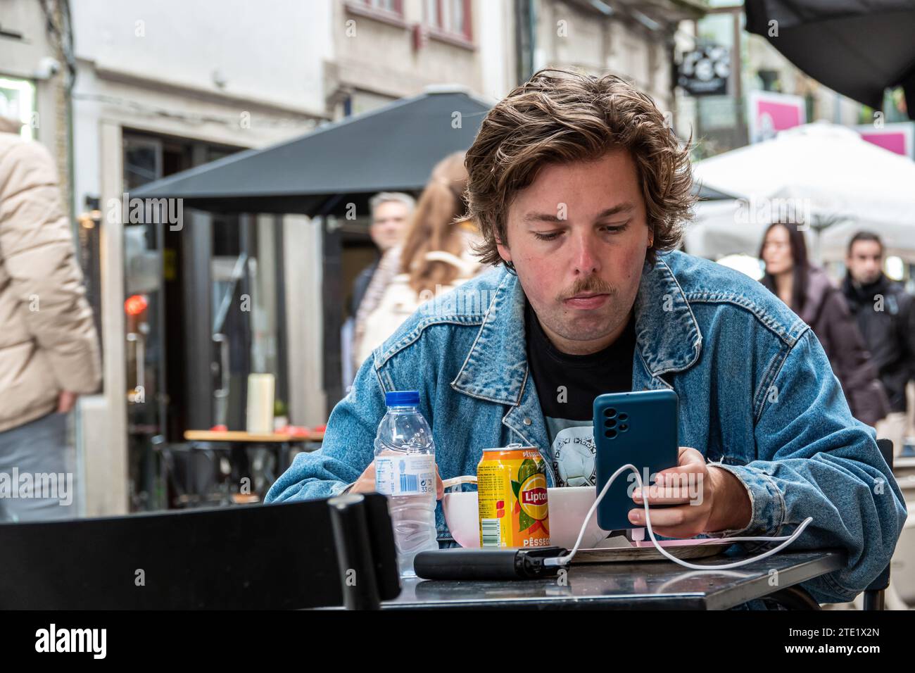 Junge, der an einem Tisch isst und auf das Handy schaut. Stockfoto