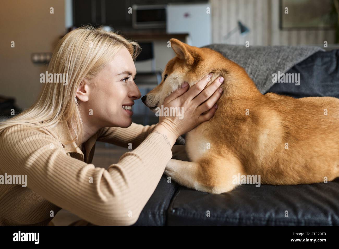 Glückliches kaukasisches Mädchen, das den Maul ihres Hundes drückt, der zu Hause auf der Couch liegt Stockfoto