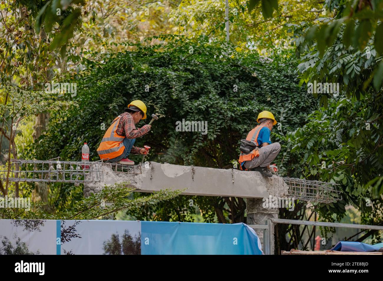 Engagierte indonesische Bauarbeiter auf einem Betonhaufen, die mit Entschlossenheit vor einem Hintergrund von Bäumen hämmern, was Fortschritt und hart symbolisiert Stockfoto