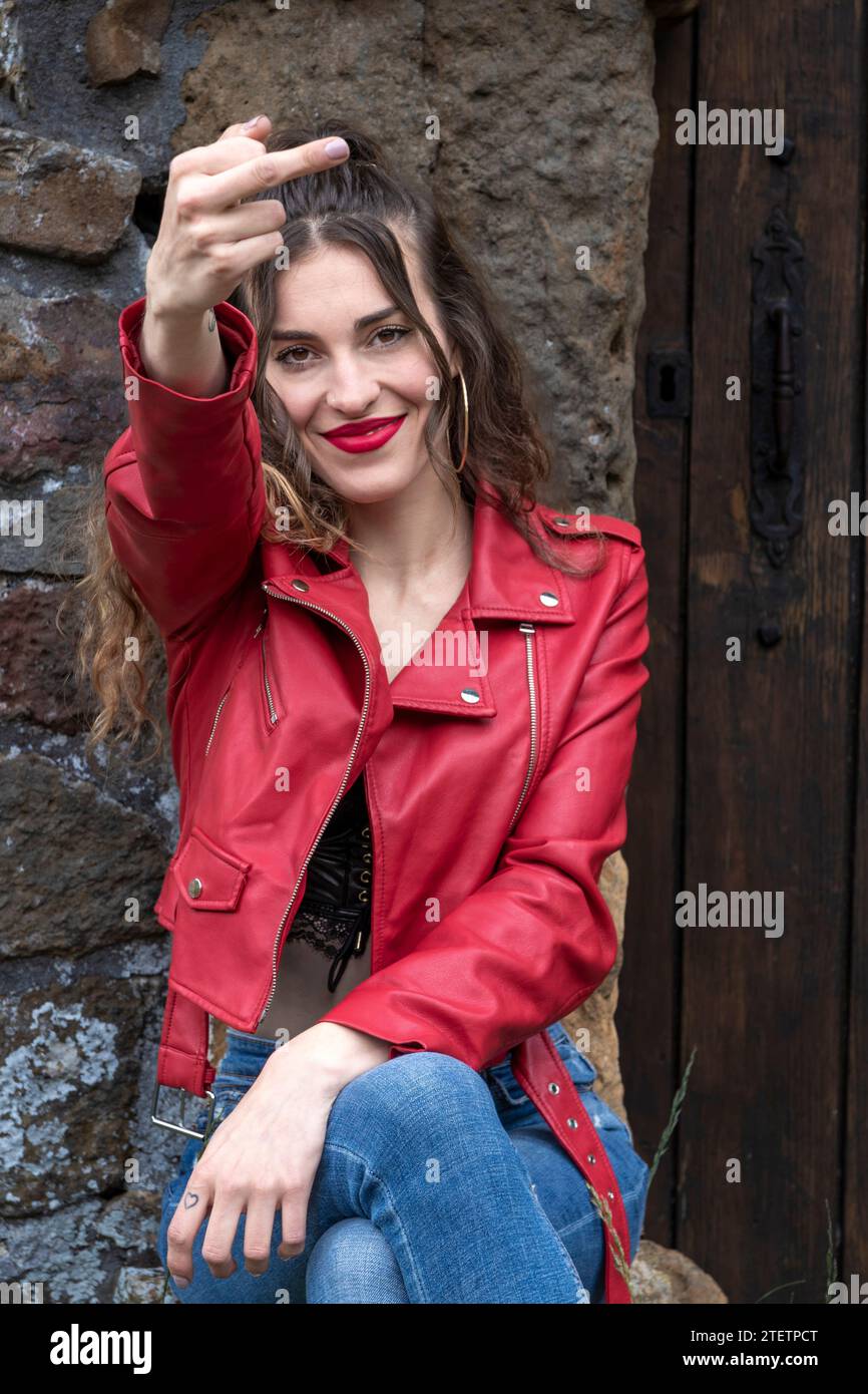 Frau in einer roten Jacke, die an einer alten Tür sitzt, Handgeste, Tattoo am Handgelenk, rustikaler Hintergrund Stockfoto