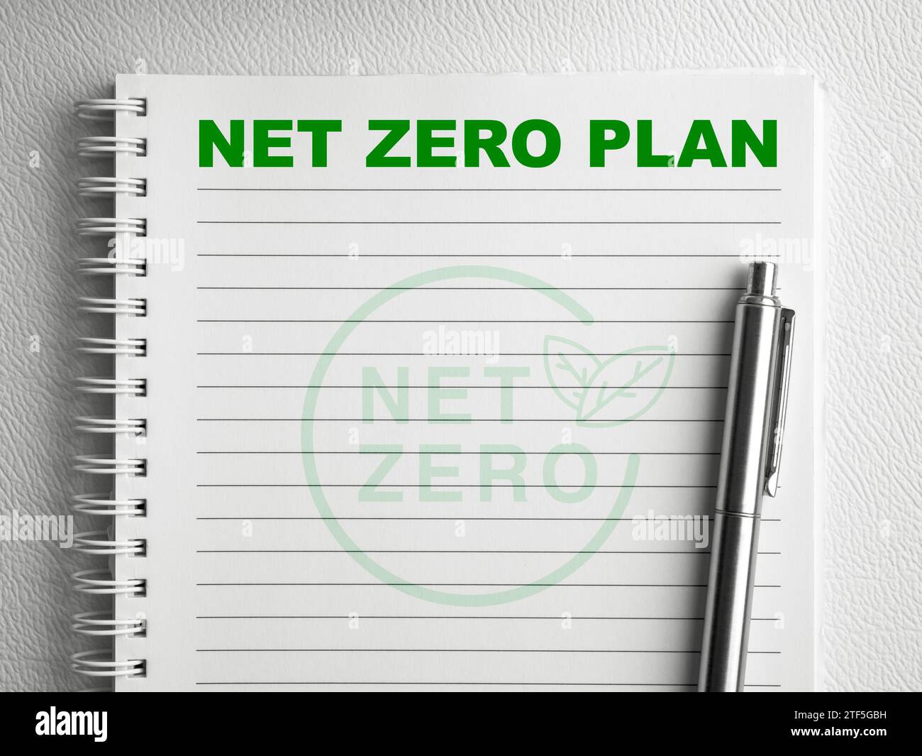 Grüner Text „Net Zero Plan“ oben auf der leeren vertikalen Notizblock-Seite mit silbernem Stift auf weißem Spiralnotizbuch. Klimaneutrale langfristige Strategie Sust Stockfoto