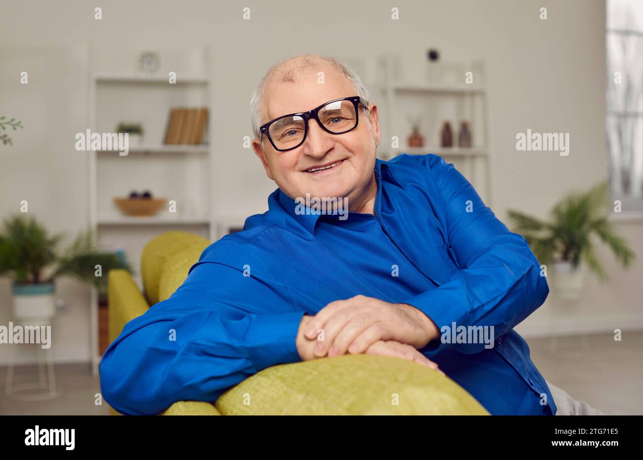 Porträt eines glücklichen, lächelnden älteren Mannes mit Brille, der zu Hause auf dem Sofa sitzt Stockfoto