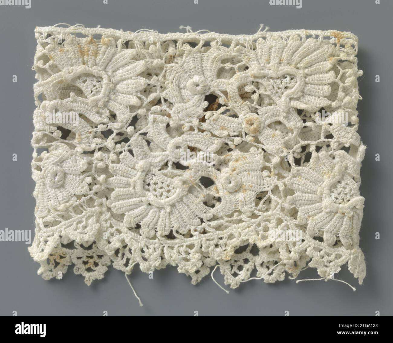 Manschette von der Häkelseite mit fächerförmigen Blüten, anonym, ca. 1890 - ca. 1909 Manschette aus natürlicher irischer Häkelseite, Nachahmung grober venezianischer Seite. Muster mit fächerförmigen Blüten mit Stielen und gehäkeltem unregelmäßigem Netzboden mit Pikots. Die Oberseite ist mit einem Lineal versehen. Die halbkreisförmigen Skulpturen am unteren Rand sind mit pikotierten Bögen versehen. Irische Baumwolle (Textil) Manschette aus natürlicher irischer Häkelseite, Nachahmung grober venezianischer Seite. Muster mit fächerförmigen Blüten mit Stielen und gehäkeltem unregelmäßigem Netzboden mit Pikots. Die Oberseite ist mit einem geraden edg versehen Stockfoto