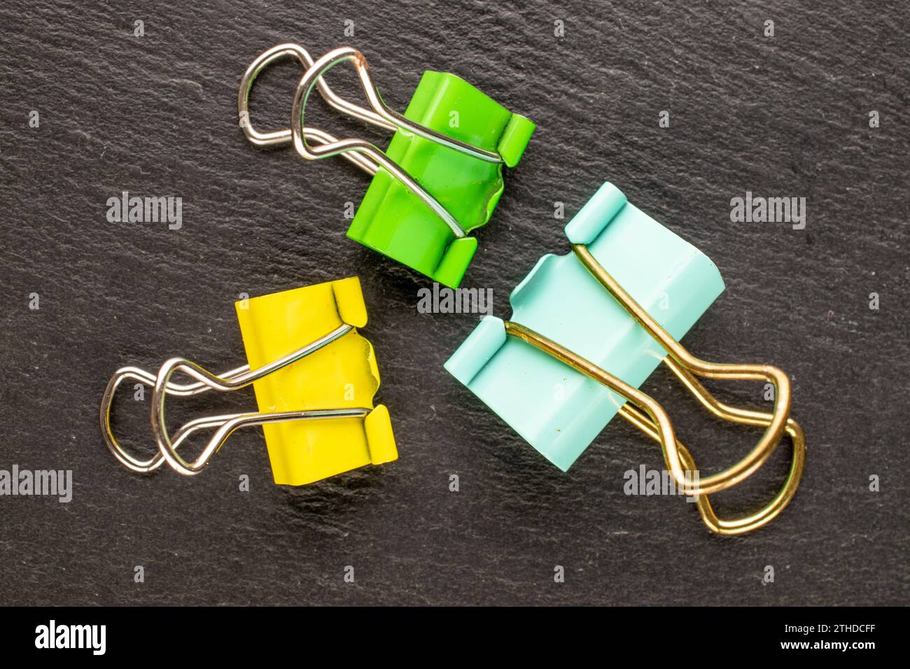 Drei Büroklammern aus Metall auf Schieferstein, Makro, Draufsicht. Stockfoto