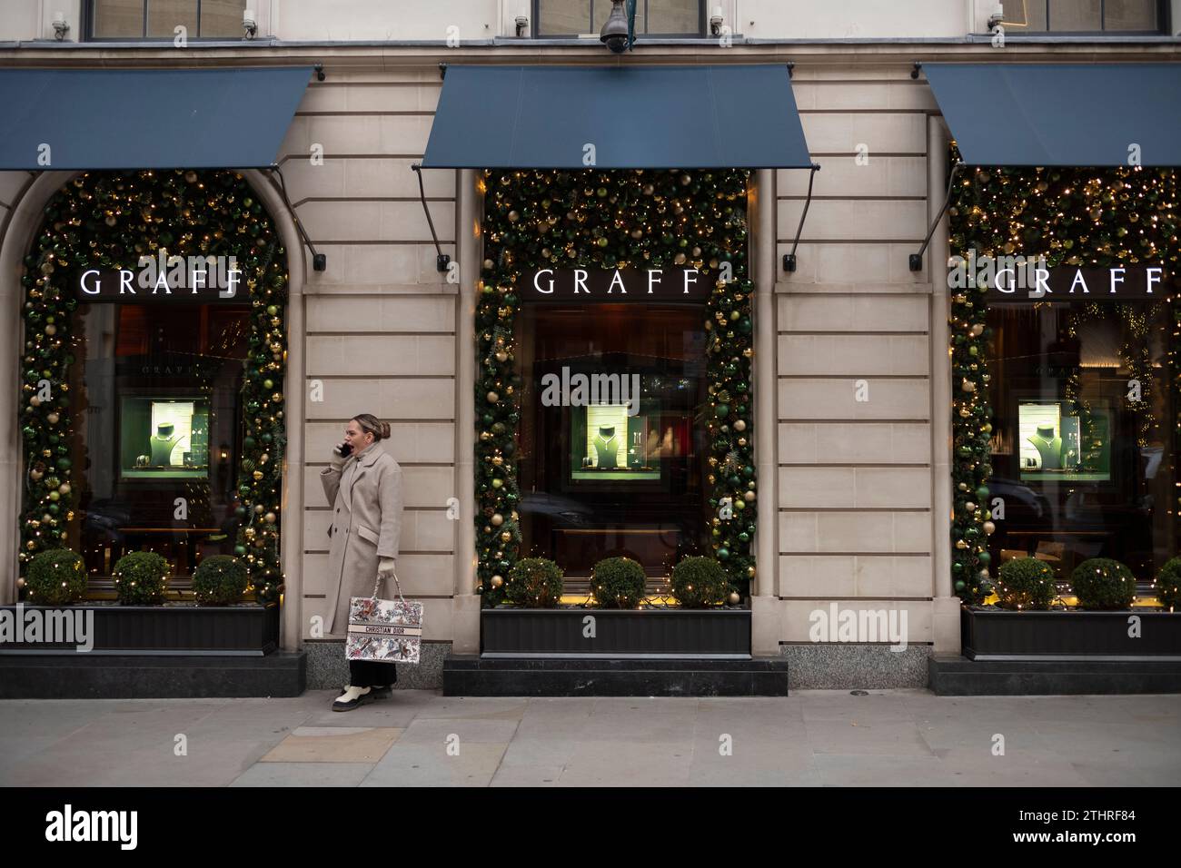 Am 20. Dezember 2023 hält eine Frau an, um zu gähnen, während sie einen Anruf auf ihrem Smartphone entgegennimmt, entlang der Old Bond Street im Herzen von Londons Mayfair. Stockfoto