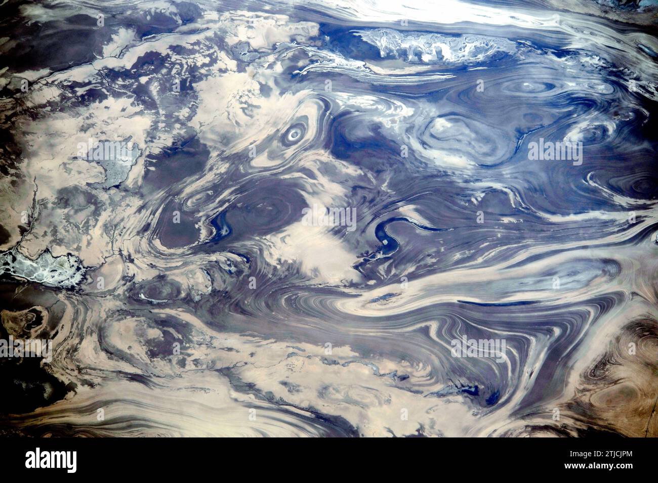 Iran. Dieses Bild wurde aufgenommen, als die Internationale Raumstation die Wüsten Zentralirans überquerte, einschließlich Kavir. Der Mangel an Boden und Vegetation ermöglicht es, die geologische Struktur der Felsen zu sehen. Die Muster ergeben sich aus der sanften Faltung zahlreicher dünner, heller und dunkler Gesteinsschichten. Das dunkle Wasser eines Sees (Mitte) nimmt eine Vertiefung in einer leicht erodierten, S-förmigen Schicht ein. Ein kleiner Fluss schlängelt sich am unteren Rand des Bildes. Es gibt nichts, was ein Gefühl von Skalierung vermitteln kann; die Bildbreite entspricht einer Entfernung von 65 km, eine optimierte Version eines Originalbildes der NASA / Credit: NASA Stockfoto