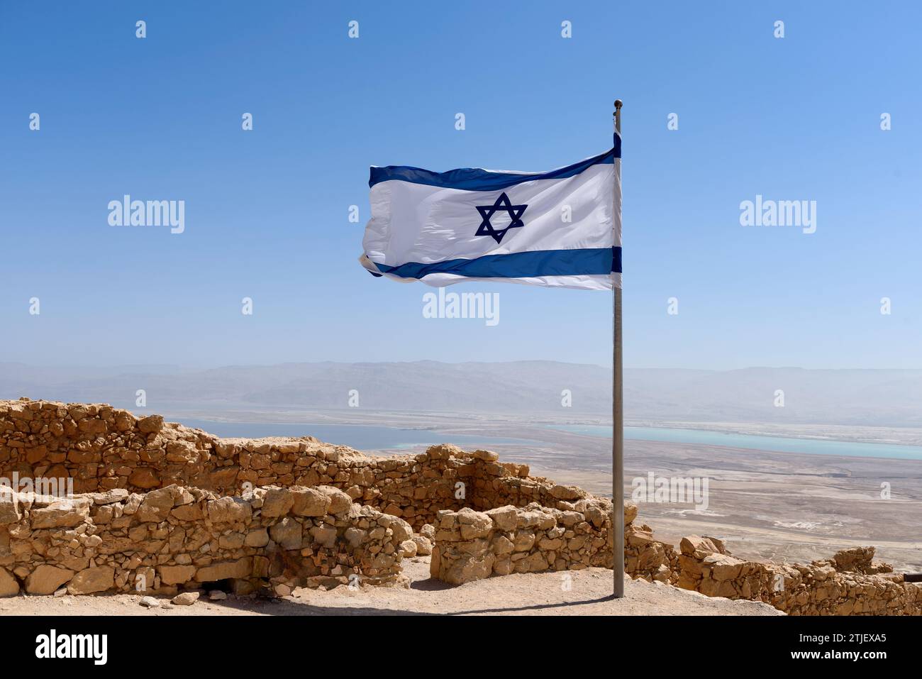 Eine israelische Flagge, die über der Festung Masada mit Blick auf das Tote Meer fliegt. Masada (Hebräisch מְצָדָה məṣādā, „Festung“; arabisch جبل مسعدة) ist eine alte Festung im südlichen Bezirk Israels, die sich auf einem abgelegenen Felsplateau befindet, ähnlich einer mesa. Es liegt am östlichen Rand der Judäischen Wüste, mit Blick auf das Tote Meer 20 km östlich von Arad. Herodes der große baute zwei Paläste auf dem Berg und befestigte Masada zwischen 37 und 31 v. Chr.. Kredit: Digitaleye/JdeSousa Stockfoto