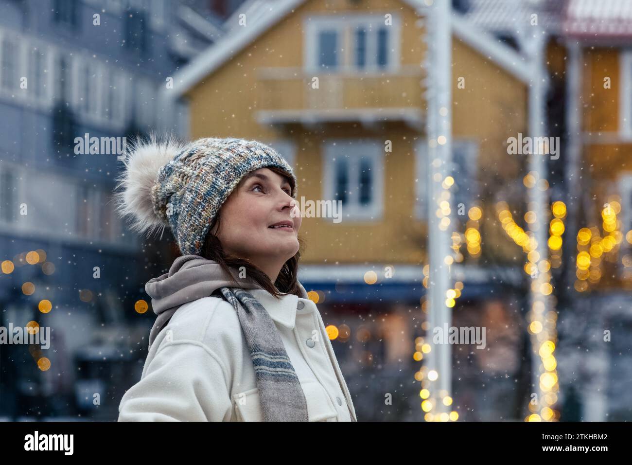 Eine lächelnde Frau in ihrer Blüte, die den Charme einer nordischen Stadt, die zu Weihnachten und Neujahr dekoriert ist, bewundert. Hochwertige Fotos Stockfoto