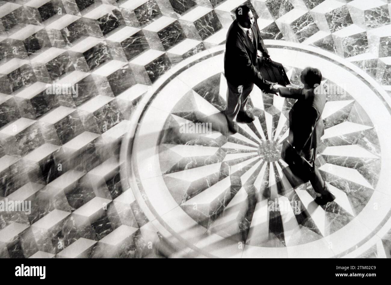 Ein Blick von oben auf zwei Geschäftsleute, die sich die Hände schütteln, während sie auf einem kunstvollen Marmorboden stehen Stockfoto