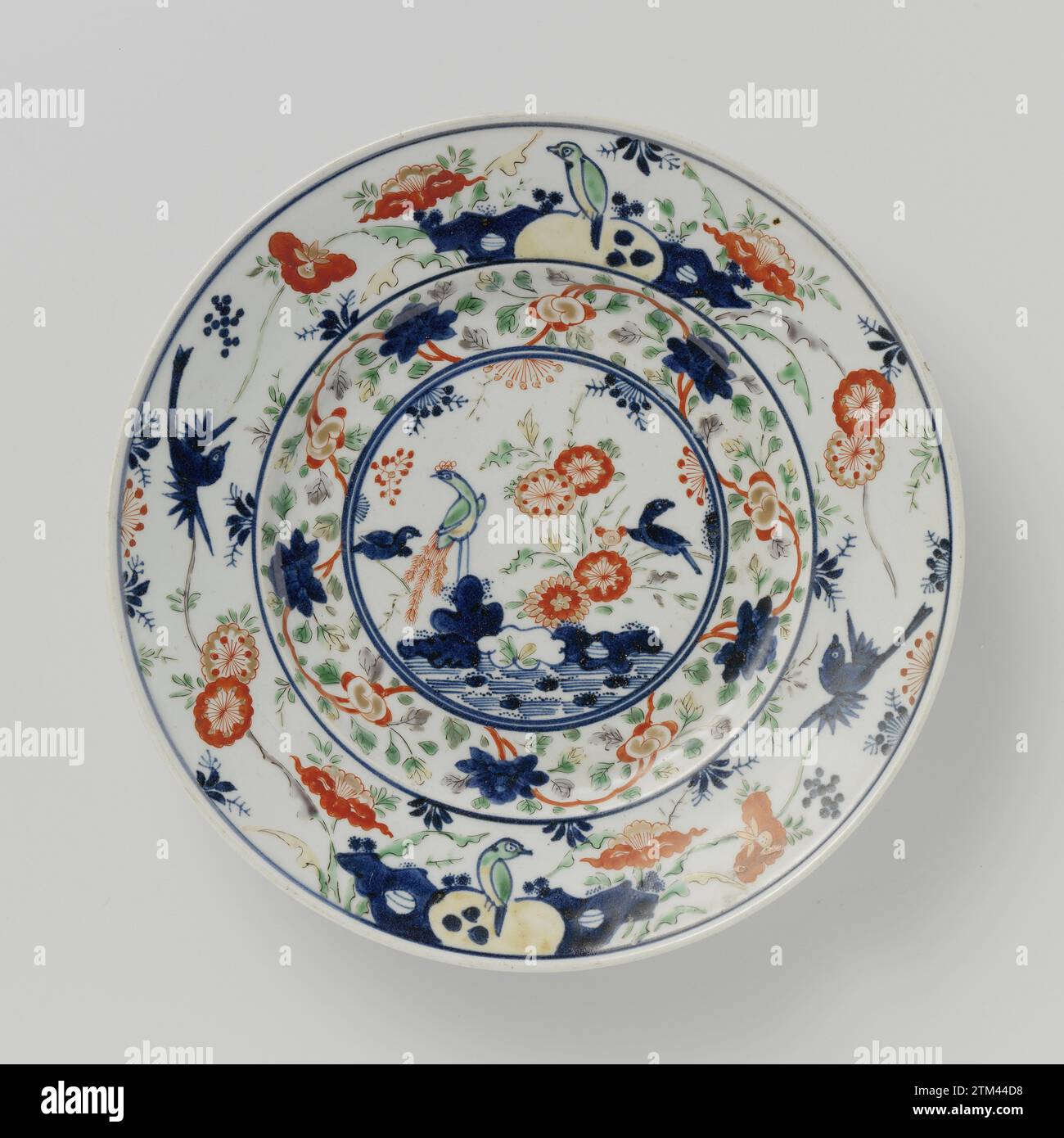 Teller mit Vögeln auf Felsen und in der Nähe blühender Pflanzen, anonym, ca. 1700 - ca. 1799 Porzellanplatte, bemalt in Unterglasur blau und auf der Glasur rot, grün und Gold. Auf der Ebene ein Medaillon mit einem Pfau auf einem Felsen in blühenden Pflanzen, einen Teich und einen fliegenden Vogel. Ein durchgehendes Blumengetränk für das Medaillon. Der Rand mit zweimal einem Vogel auf einem Felsen mit blühenden Pflanzen mit einem fliegenden Vogel dazwischen. Vier Pronen auf dem Boden. Imari. Japanisches Porzellan. Glasur. Kobalt (Mineral). Gold (Metall) Malerei / Vergoldung / Vitrifikation Porzellanplatte, lackiert in Unterglasur blau und auf der Glasur rot, grün und Stockfoto