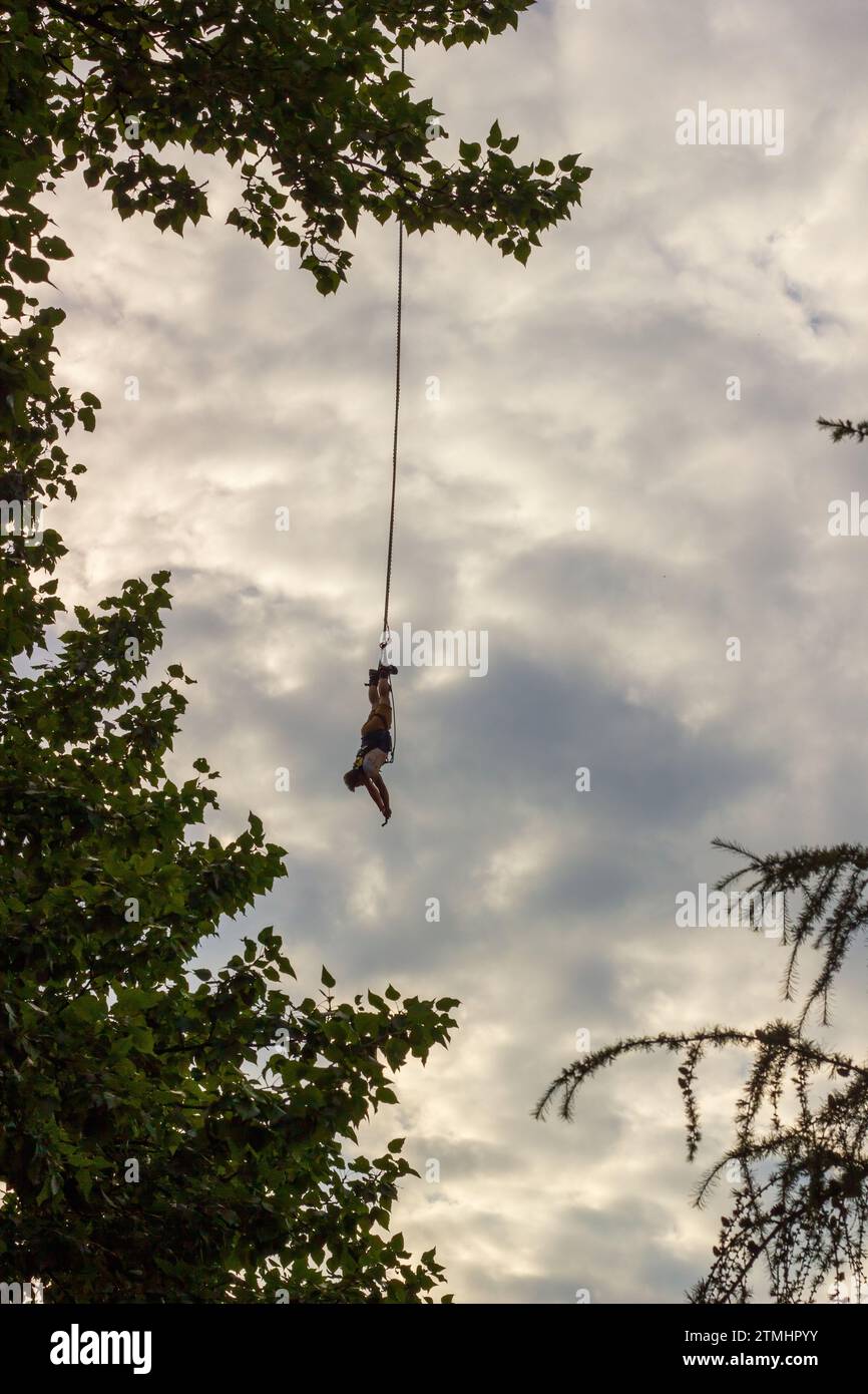 Ein Mann, der kopfüber an ein Seil gebunden ist, macht einen Bungee-Sprung, während er eine Action-Kamera hält Stockfoto