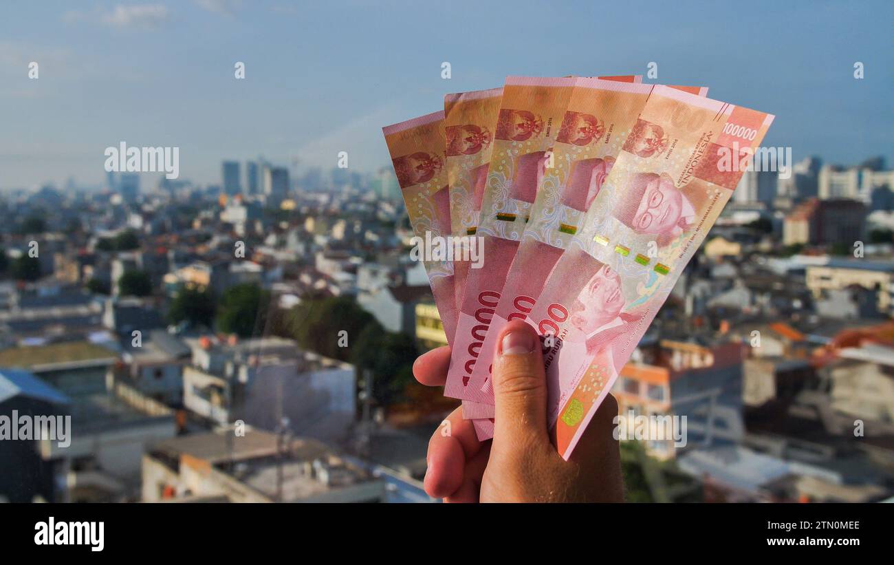 Die Hand des Mannes hält Rupiah-Geld vor dem Hintergrund der Hauptstadt Indonesiens. Stockfoto