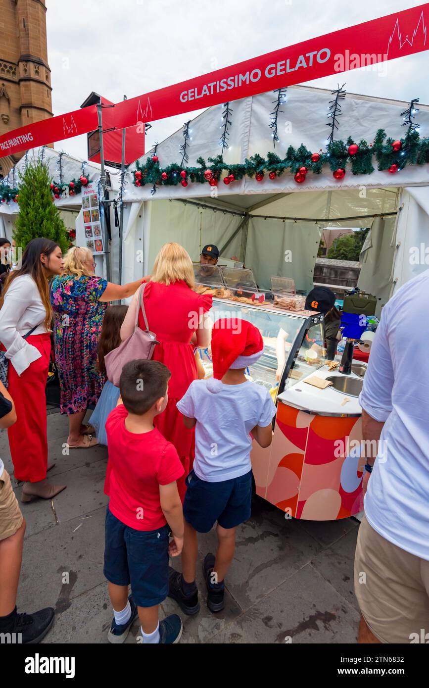 Menschen in rot-weißen Weihnachts-Outfits stellen sich an einer heißen Weihnachtsnacht in Sydney, Australien, für ein kühlendes Eis an Stockfoto