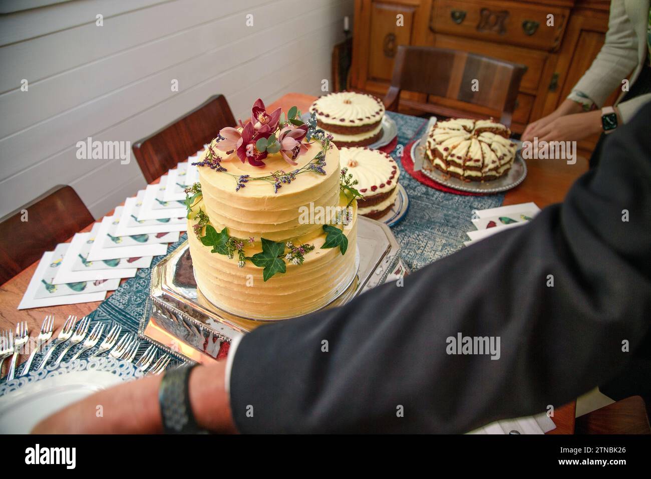 Ein Mann, der nach Tellern greift, neben einem Holztisch mit wunderschönen Bohemian-Kuchen auf einer Hochzeit Stockfoto