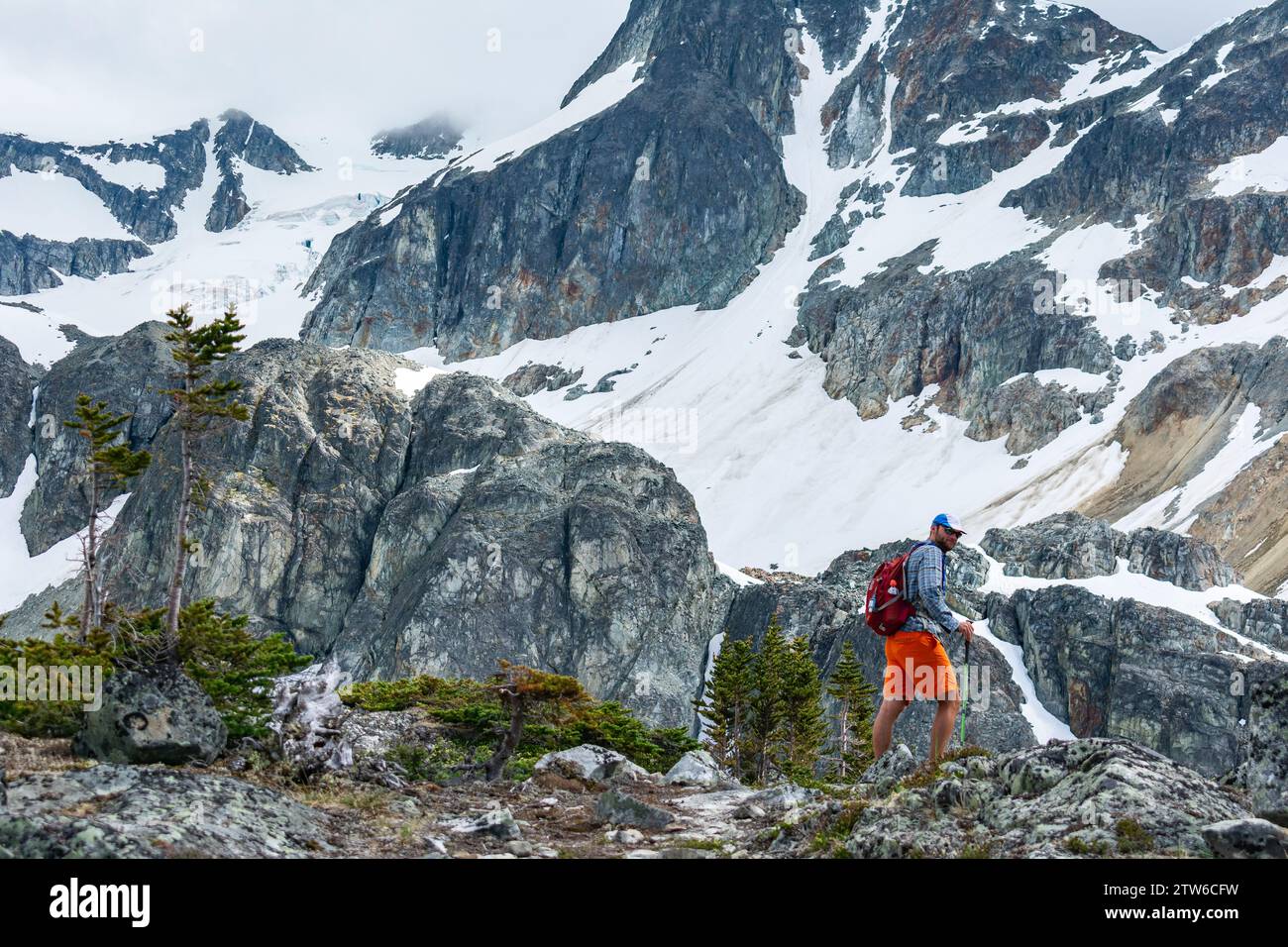 Ein einsamer Wanderer durchquert das zerklüftete alpine Gelände der Kanadischen Rocky Mountains, umgeben von majestätischen schneebedeckten Gipfeln. Stockfoto