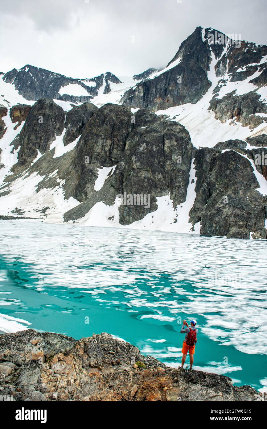 Ein überschwänglicher Wanderer feiert die eisige Weite des Wedgemount Lake inmitten der kanadischen Gipfel. Stockfoto