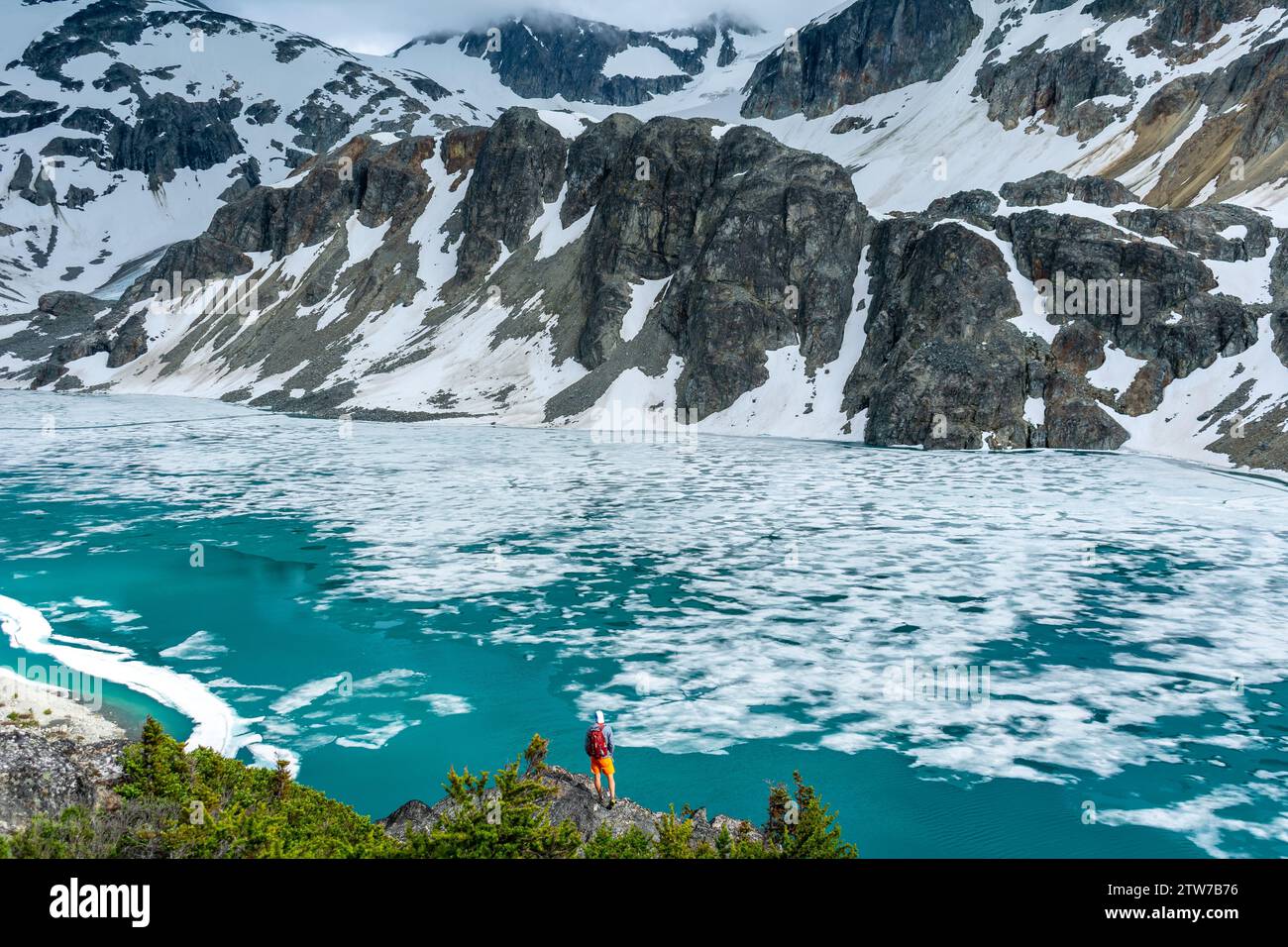 Wanderer in roter Jacke stehen auf dem Wedgemount Lake Trail inmitten eines atemberaubenden Gletscherpanoramas in Ehrfurcht. Stockfoto