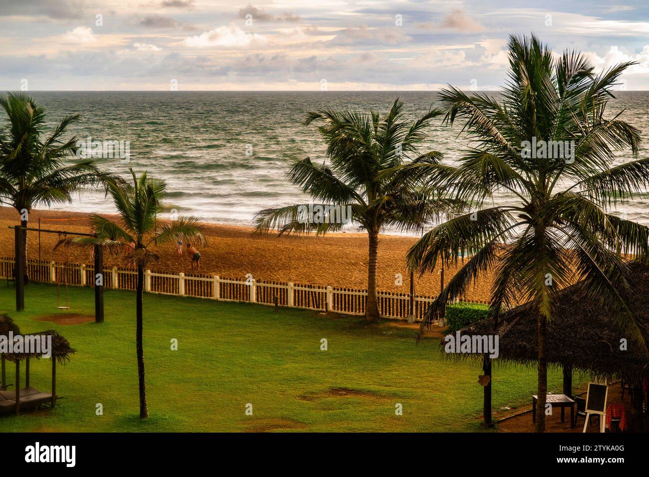 Garten mit Palmen, welliges Indisches Meer, bewölkter Himmel vor dem Abendmonsun. Die Leute spielen Beachvolleyball. Waskaduwa, Sri Lanka. Stockfoto