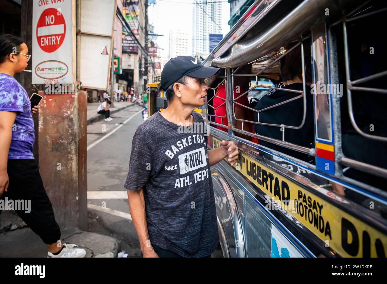 Ein philippinischer Mann läuft an der Seite eines Jeepney entlang. Ich bin mir ehrlich nicht sicher, ob er Geld für Fahrgeschäfte oder Betteln sammelte. Stockfoto