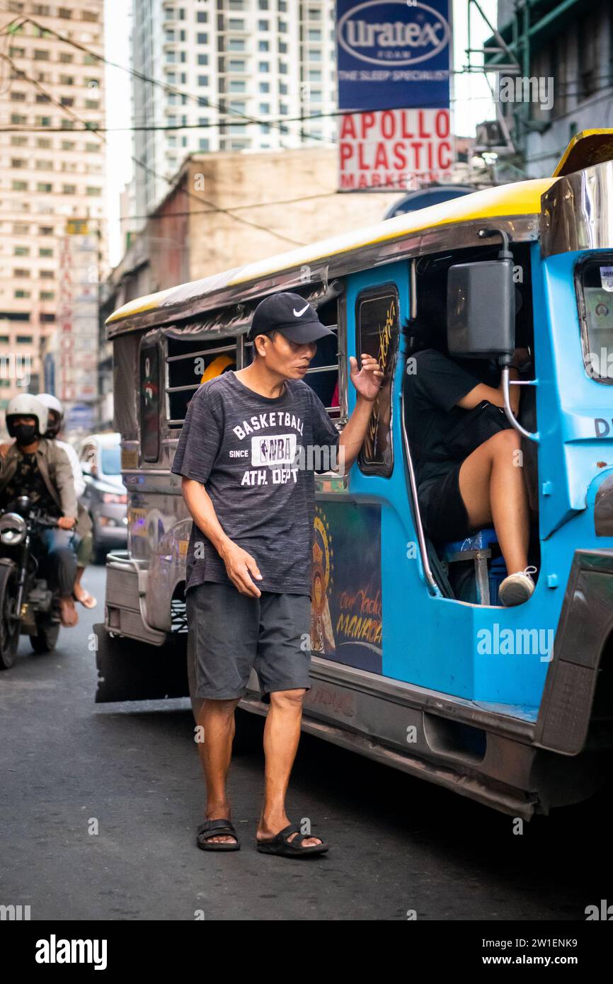 Ein philippinischer Mann läuft an der Seite eines Jeepney entlang. Ich bin mir ehrlich nicht sicher, ob er Geld für Fahrgeschäfte oder Betteln sammelte. Stockfoto