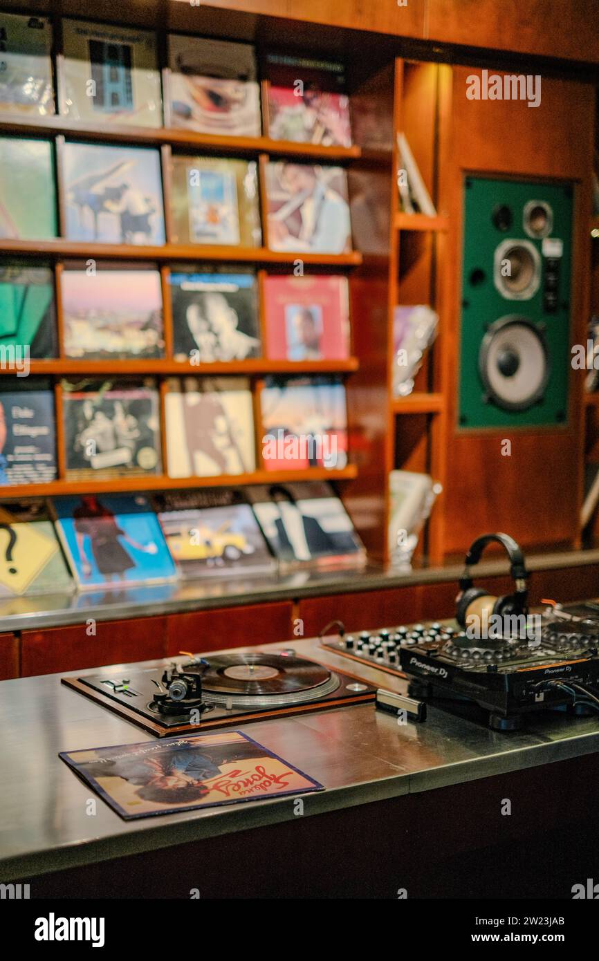 Versetzen Sie sich in eine vergangene Zeit mit einem körnigen, porträtähnlichen Blick auf ein Café. Vintage-Platten säumen die Hintergrundwand, und ein klassisches Rec Stockfoto