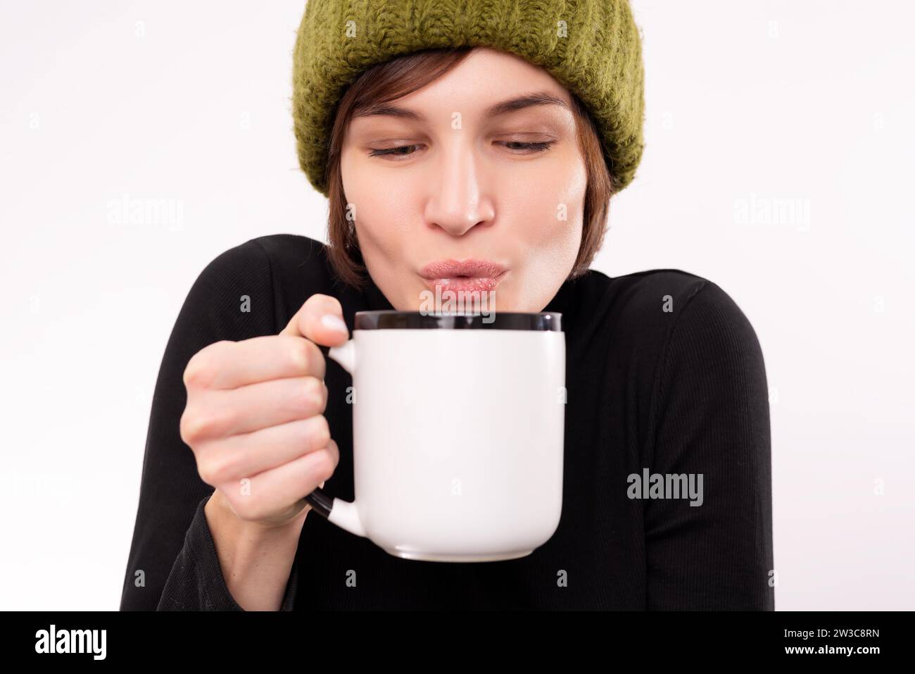 Porträt einer Frau in grünem Strickmütze mit einem Becher in den Händen. Saisonales Viruskrankheitskonzept. Gemischte Medien Stockfoto