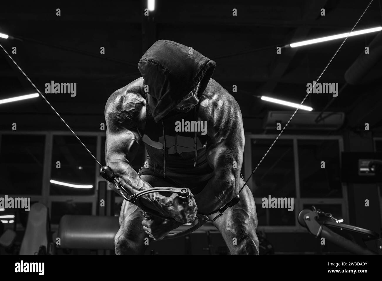 Bild eines leistungsstarken Athleten in einem Hoodie, der in einer Crossover-Übung im Fitnessstudio trainiert. Fitness- und Bodybuilding-Konzept. Gemischte Medien Stockfoto