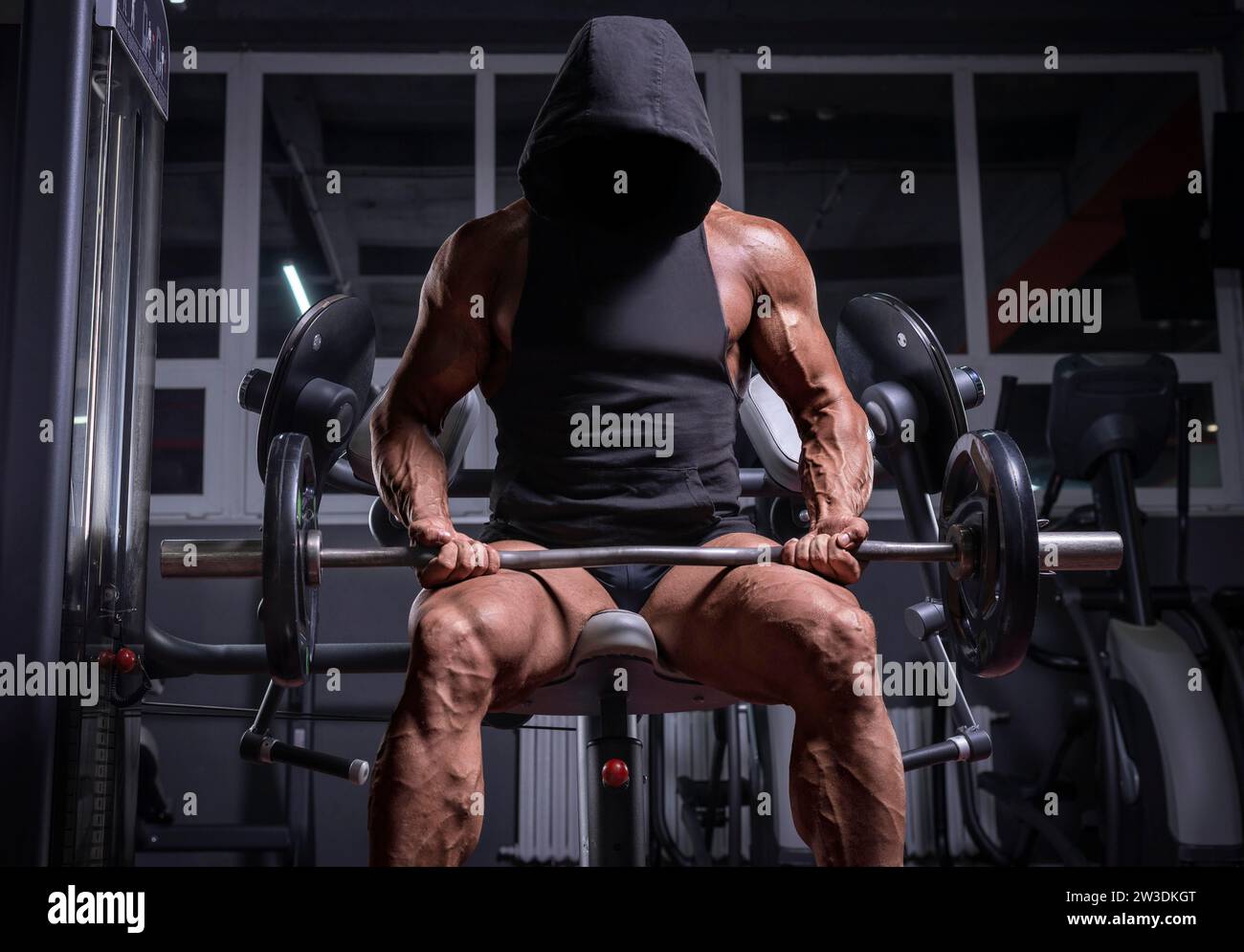 Kein Name Bild eines mächtigen Athleten in einem Hoodie, der auf einer Bank in einem Fitnessstudio sitzt. Fitness- und Bodybuilding-Konzept Stockfoto
